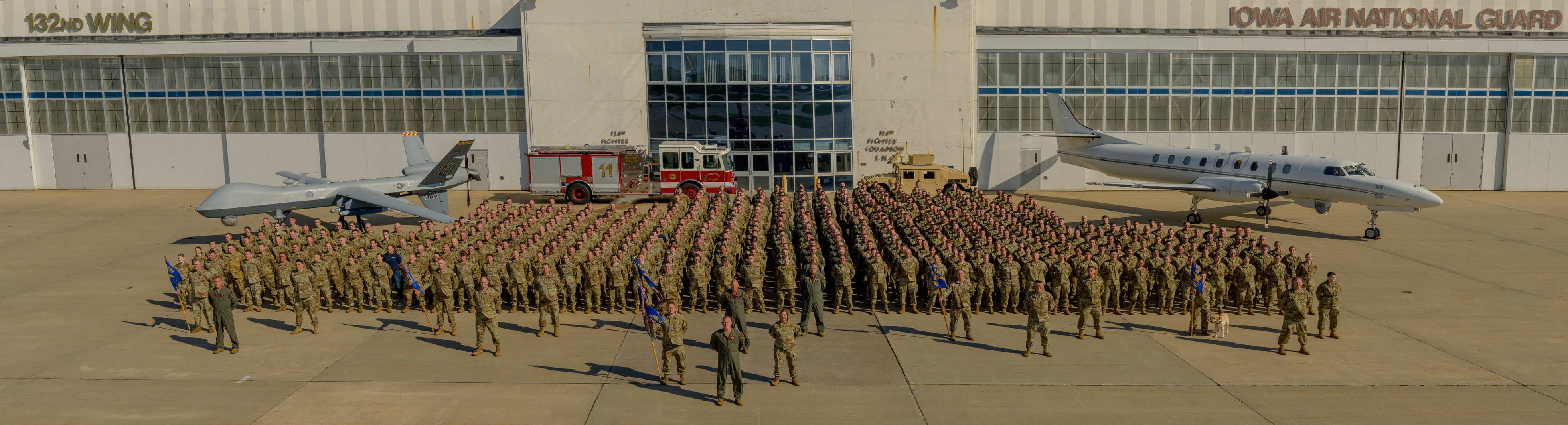 A large group of Airmen stand in formation for a group photo with aircraft in the background